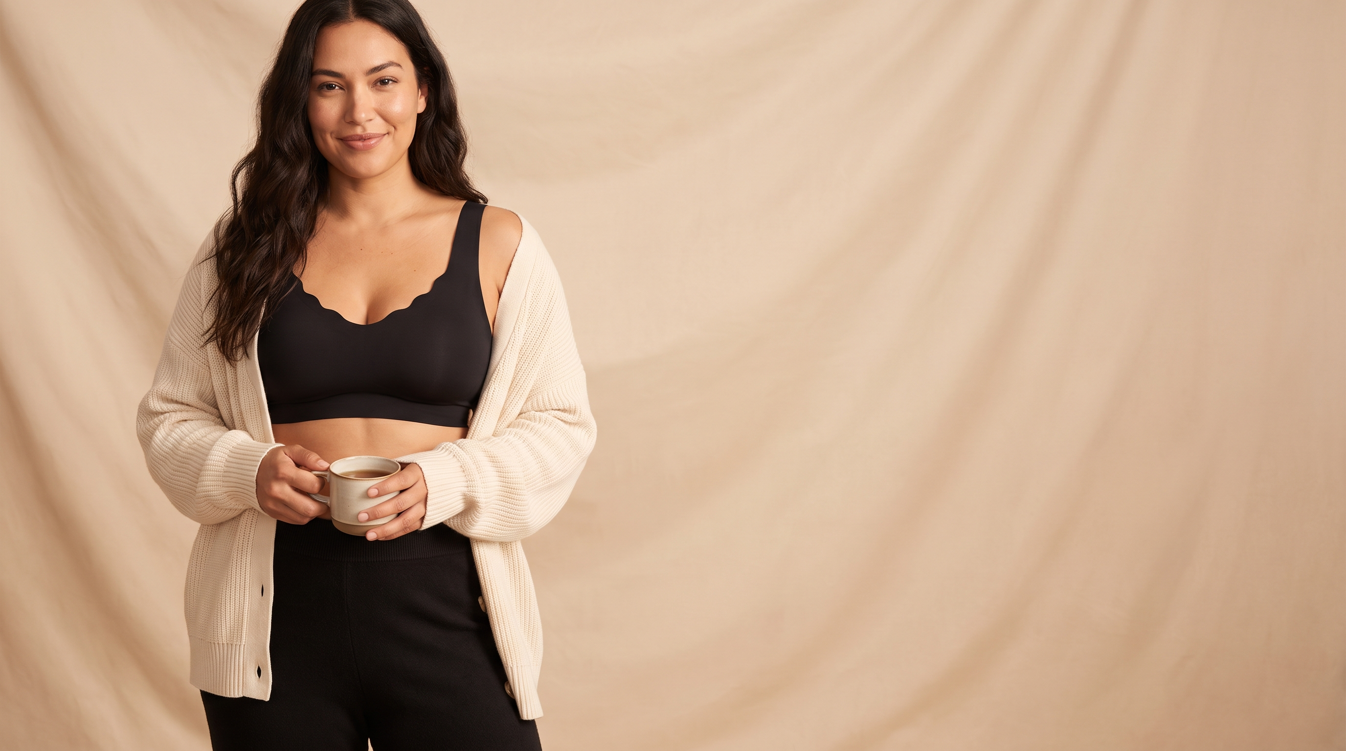 Woman in a cream cardigan wearing the black Sonist Jelly Bra holding a mug of tea against a warm beige backdrop